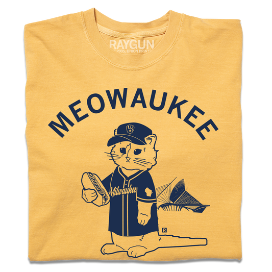 A folded mustard yellow t-shirt with navy ink that says, "MEOWAUKEE" in curved text over Gary The Cat wearing Brewers gear while holding a hotdog.