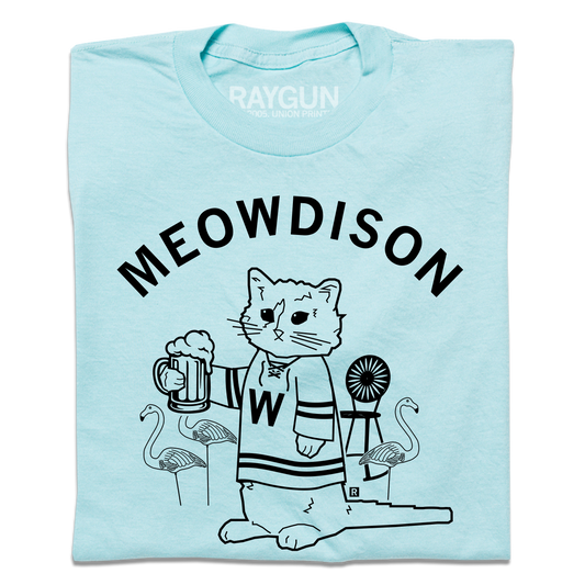 A folded pastel blue t-shirt with black ink. Curved text at the top says, "Meowdison" above an illustration of a cat holding a pint of beer while wearing a hockey jersey. There are lawn flamingos and a rocking chair in the background.
