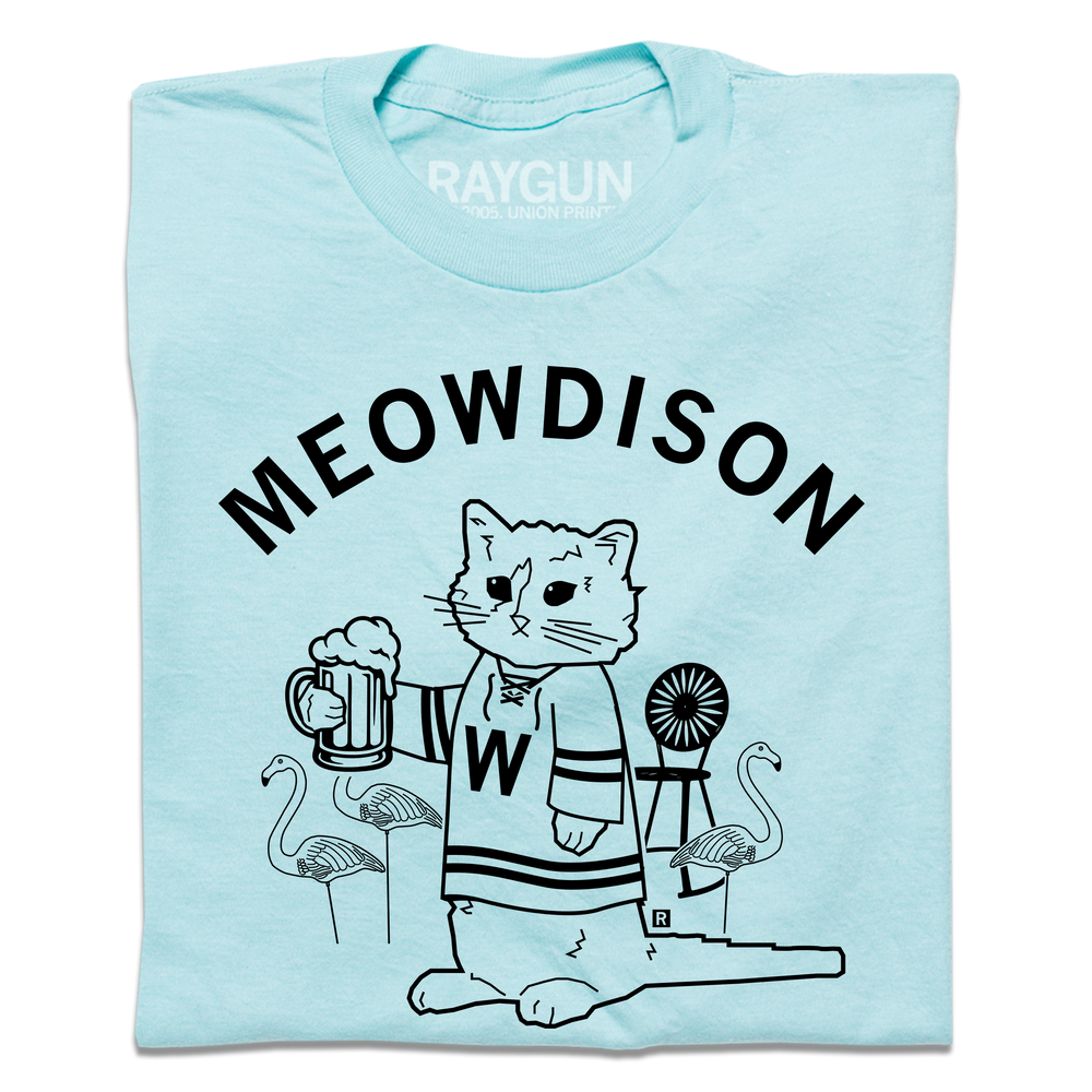 A folded pastel blue t-shirt with black ink. Curved text at the top says, "Meowdison" above an illustration of a cat holding a pint of beer while wearing a hockey jersey. There are lawn flamingos and a rocking chair in the background.