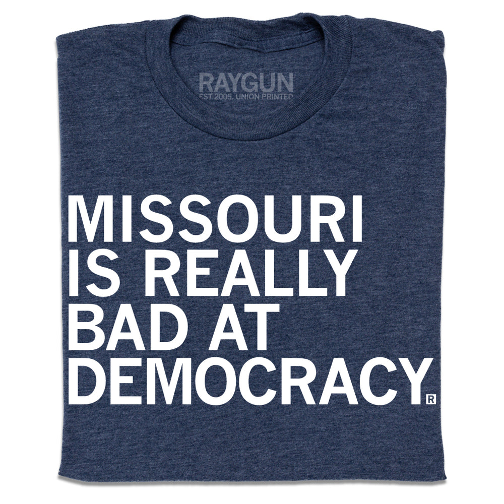 A folded heather navy t-shirt with left-aligned white ink text that says, "Missouri is really bad at democracy" in all caps.