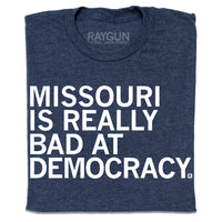 A folded heather navy t-shirt with left-aligned white ink text that says, "Missouri is really bad at democracy" in all caps.