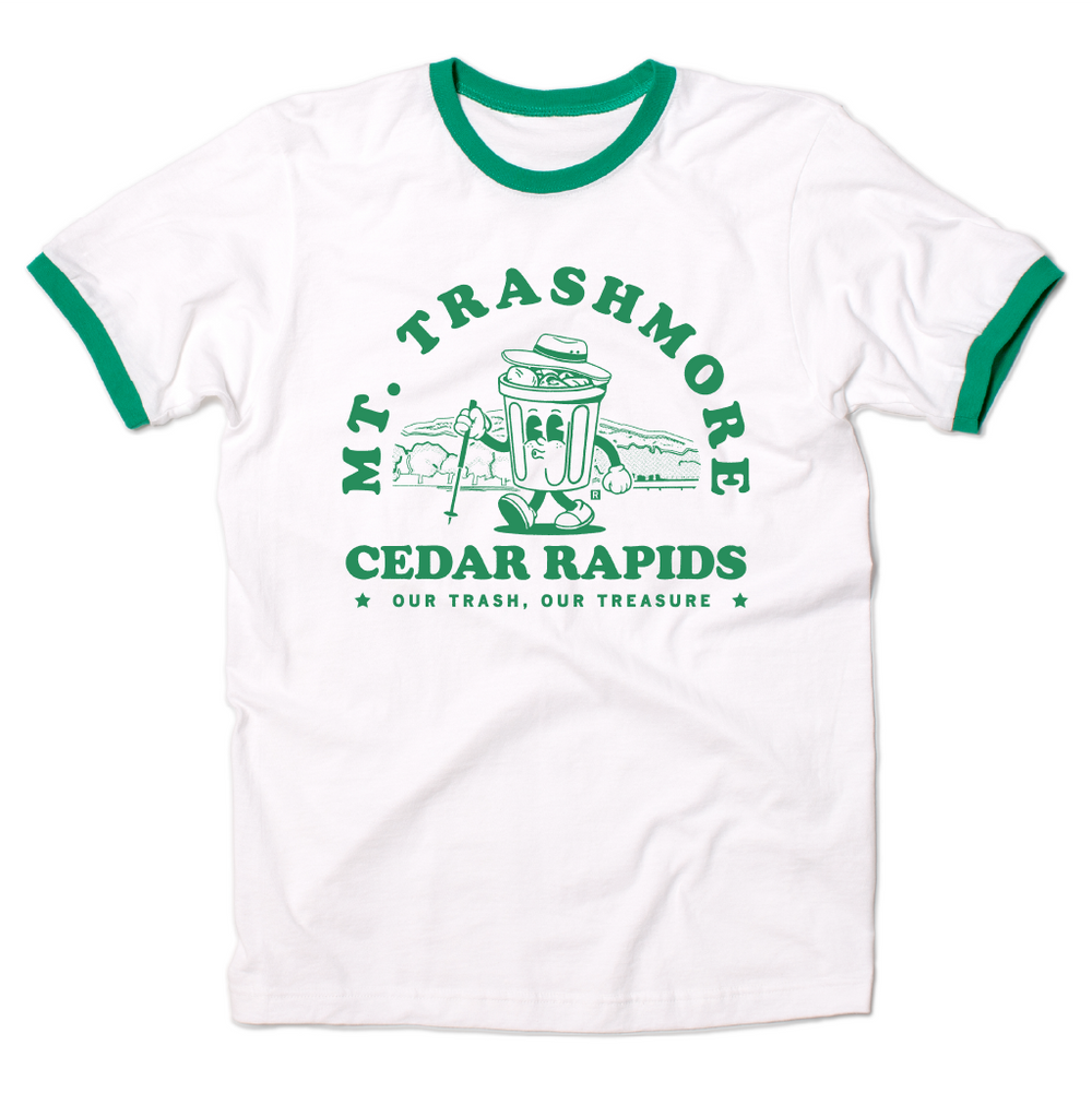 White ringer shirt with green accents and green ink that reads "Mt. Trashmore, Cedar Rapids. Our trash, our treasure" framing an image of a cartoon trashcan going for a hike with Mt. Trashmore in the background.