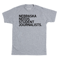 A heather grey short sleeved t-shirt with left aligned black in text that reads "Nebraska Needs Student Journalists"