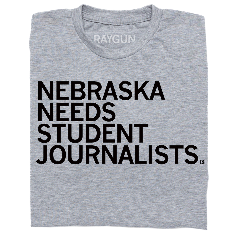 A folded heather grey t-shirt with left aligned black in text that reads "Nebraska Needs Student Journalists"