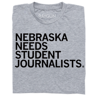 A folded heather grey t-shirt with left aligned black in text that reads "Nebraska Needs Student Journalists"