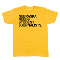 A heather mellow yellow short sleeved t-shirt with left aligned black in text that reads "Nebraska Needs Student Journalists"