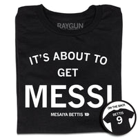 A folded short sleeve black t-shirt with centered white ink print that reads "It's About to Get Messi" with smaller text below that says, "Mesaiya Bettis" beside a small outline of Iowa with the number 9 in it. A second picture in a small circle frame is in the bottom right corner, showing the back print. The back is laid out like a jersey with "Bettis" printed across the shoulders above the number 9.