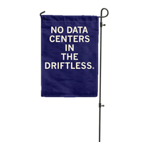 A dark blue garden flag hanging vertically from a flag pole with white ink text that says, "No data centers in The Driftless."