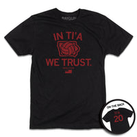 Short-sleeve black t-shirt with red ink print depicting Iowa in the center with a volleyball taking up most of the state. Text above and below Iowa says, "IN TI'A WE TRUST" with "NAYELI TI'A" in smaller  print below. Beside her name is a tiny Iowa with the number 20 in it and at the bottom of the print is the flag for Samoa. A circular image in the bottom right shows the back print. The back is laid out like a jersey with "TI'A" printed above 20.