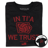Folded black t-shirt with red ink print depicting Iowa in the center with a volleyball taking up most of the state. Text above and below Iowa says, "IN TI'A WE TRUST" with "NAYELI TI'A" in smaller  print below. Beside her name is a tiny Iowa with the number 20 in it and at the bottom of the print is the flag for Samoa. A circular image in the bottom right shows the back print. The back is laid out like a jersey with "TI'A" printed above 20.