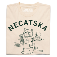 A folded cream t-shirt with dark green ink. Curved text across the top says, "Necatska" above an illustration of RAYGUN's cat mascot wearing a t-shirt that reads "the good life" along with a Nebraska necklace. He's holding on ear of corn in his right end and rural Nebraska landscape is behind him.