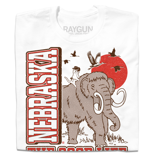 White Nebraska t-shirt with a screen print of a cat in a cowboy hat riding a woolly mammoth, set against a red sun and birds with the state name in large brown font.