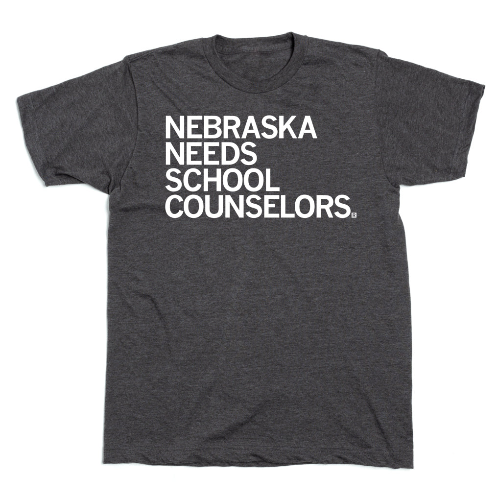 Dark gray RAYGUN t-shirt featuring the text NEBRASKA NEEDS SCHOOL COUNSELORS in white lettering on the chest.