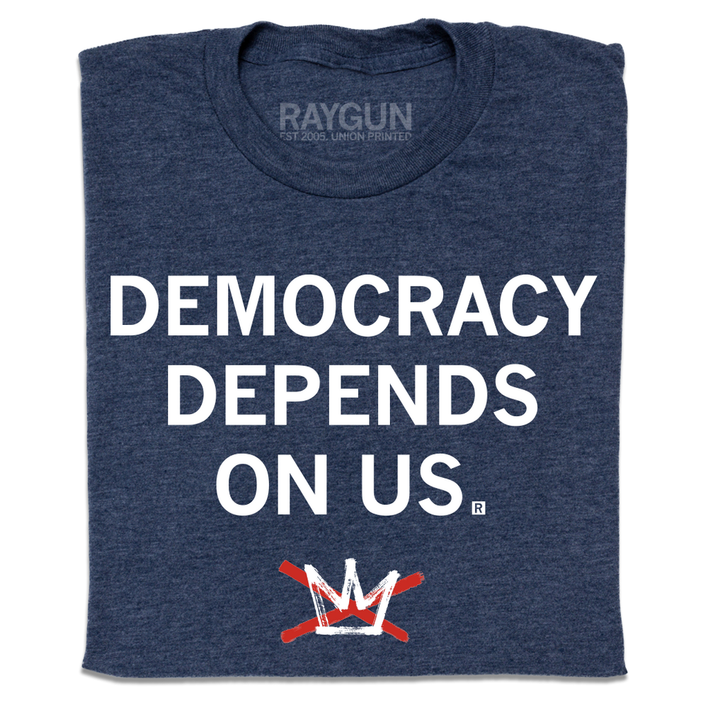 A folded heather navy t-shirt with centered white ink text that reads "Democracy Depends On Us" above the No Kings logo.