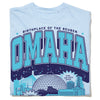Light blue garment-dyed heavyweight cotton t-shirt with a graphic that reads Birthplace of the Reuben and Omaha, featuring city skyline illustrations and a speech bubble that says Your zoo could never.