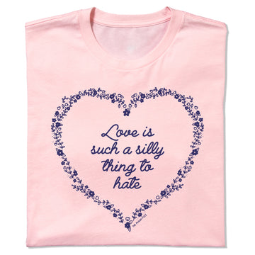 A light pink RAYGUN t-shirt featuring a dark blue floral heart outline surrounding the text Love is such a silly thing to hate.