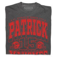A folded asphalt shirt with bright red ink that reads "Saint Patrick of Kansas City. Patrick Mahomes #15. There's No Place Like Mahomes" over an illustration of a football field with a football helmet to either side.
