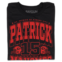 A folded black shirt with bright red ink that reads "Saint Patrick of Kansas City. Patrick Mahomes #15. There's No Place Like Mahomes" over an illustration of a football field with a football helmet to either side.