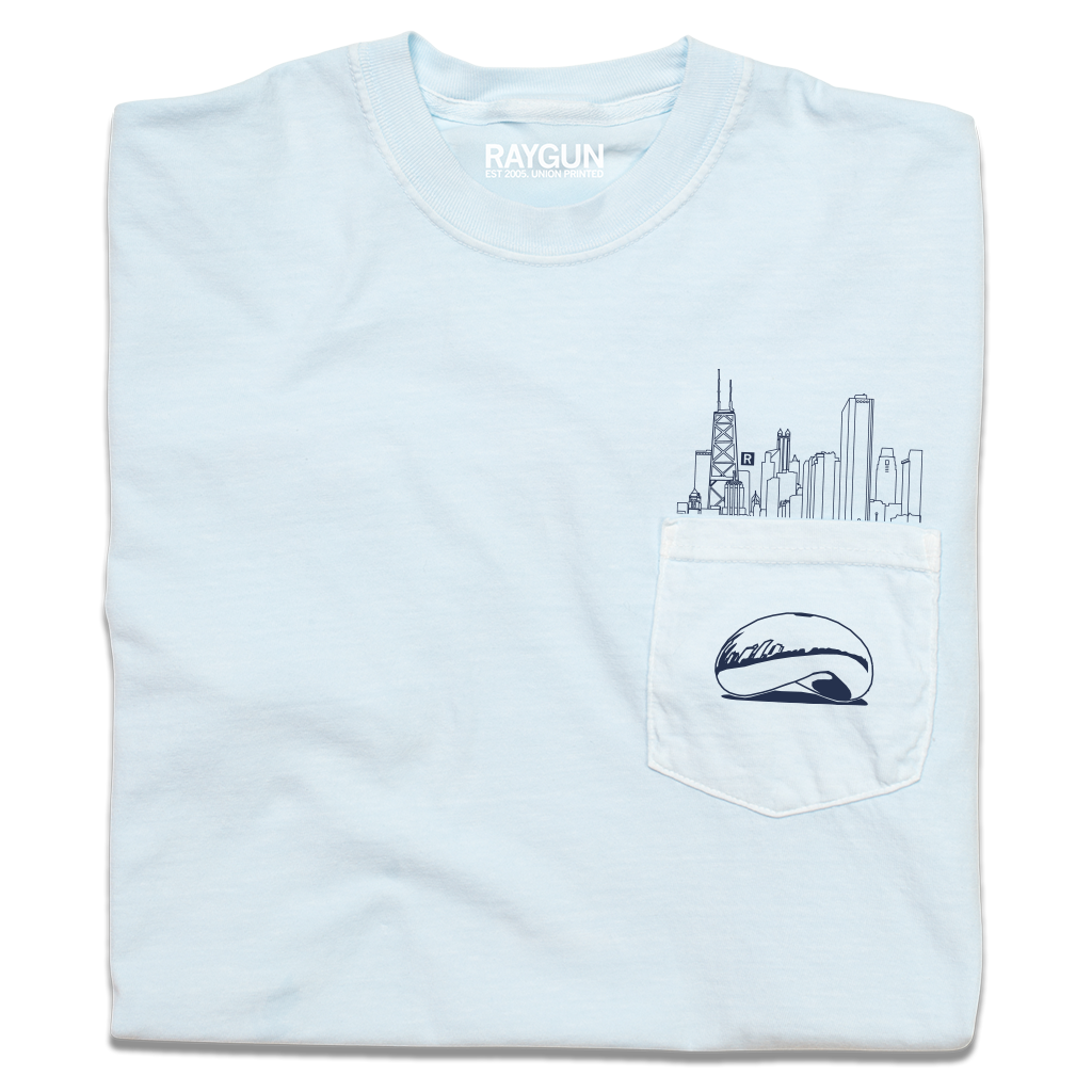 A folded light blue pocket t-shirt with navy ink. An illustration of the Chicago skyline is printed above the pocket with the Cloud Gate statue printed on the pocket.