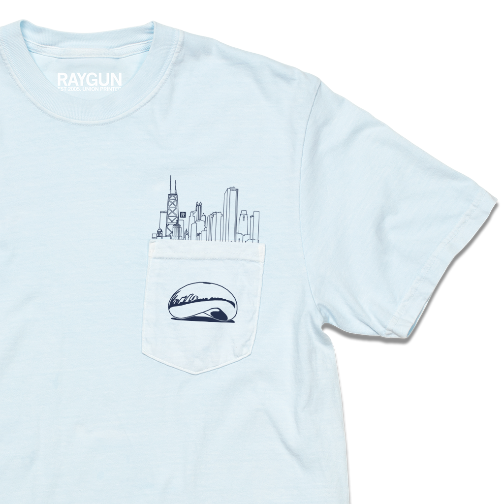 Zoom in of a light blue pocket t-shirt with navy ink. An illustration of the Chicago skyline is printed above the pocket with the Cloud Gate statue printed on the pocket.