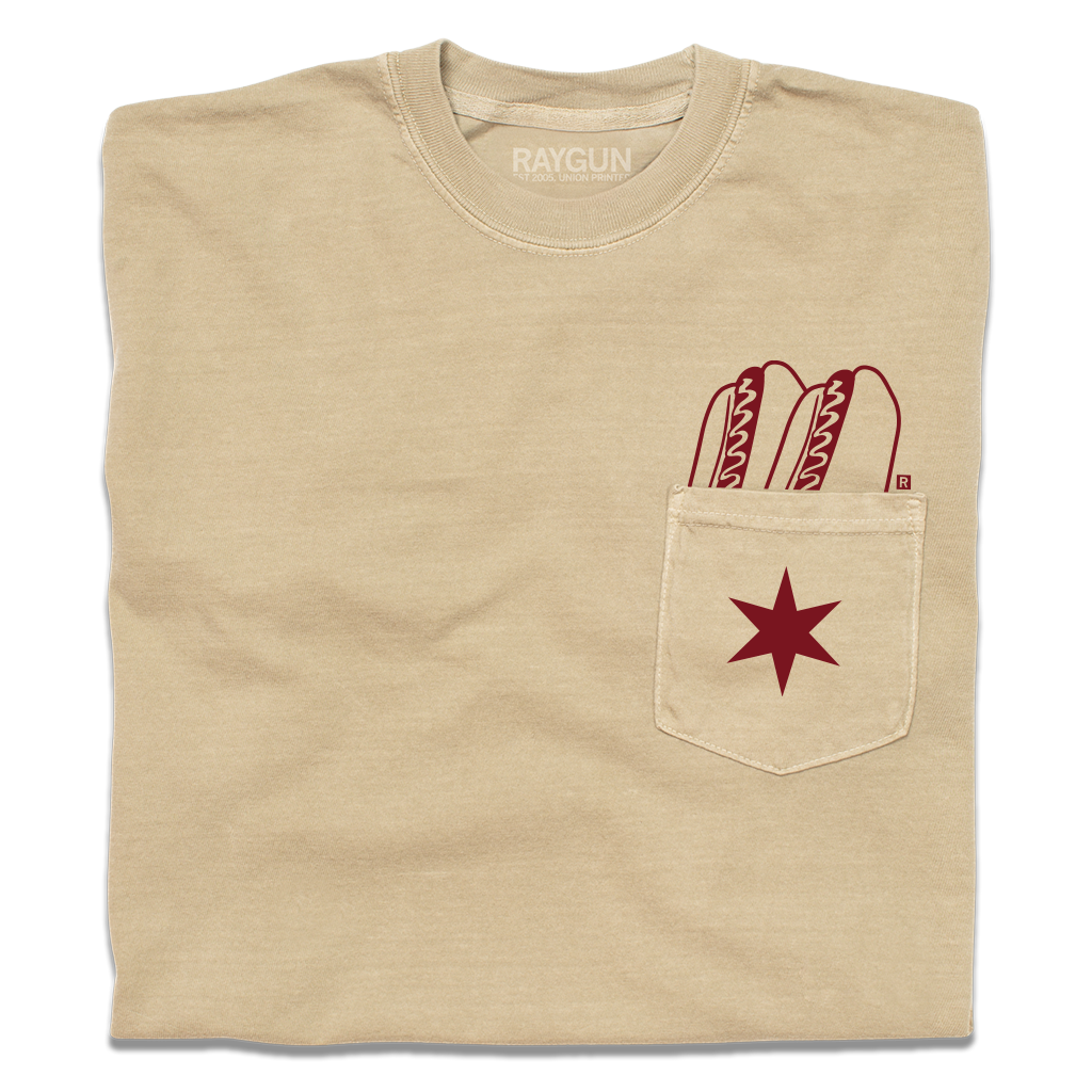 A folded beige pocket tee with dark red print of two hotdogs above the pocket and a Chicago flag star on the pocket.