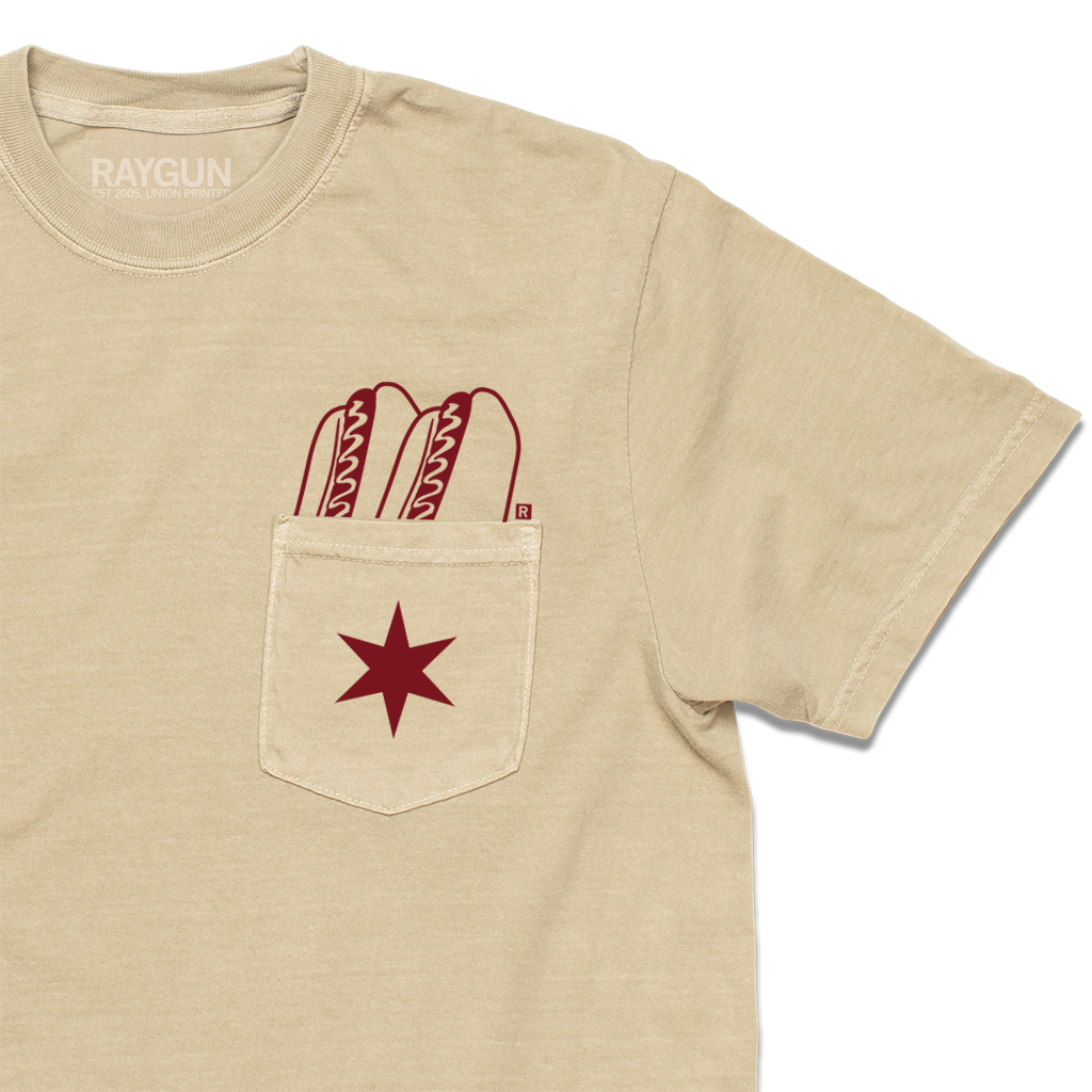 Zoom in view of a beige pocket tee with dark red print of two hotdogs above the pocket and a Chicago flag star on the pocket.