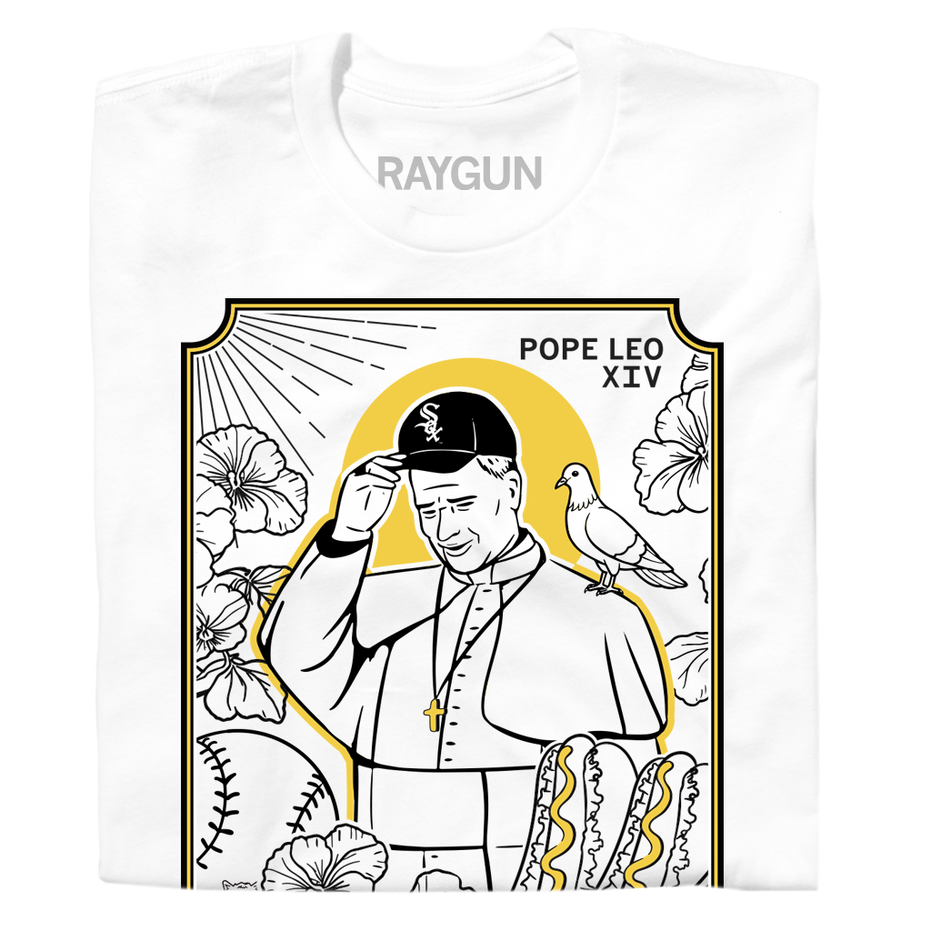 A folded white shirt with gold and black ink depicting Pope Leo wearing a White Sox hat with a pigeon on his shoulder. He's surrounding by Chicago style hotdogs, baseballs, and flowers. Black text in the top right corner says, "POPE LEO XIV" and at the bottom reads "GOD'S FAVORITE SOX FAN."