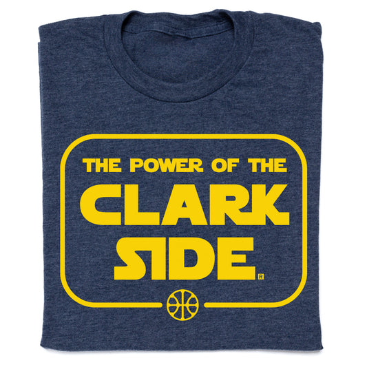 A heather denim t-shirt with gold screen print text reading The Power of the Clark Side inside a rounded yellow rectangle, featuring a basketball icon at the bottom.