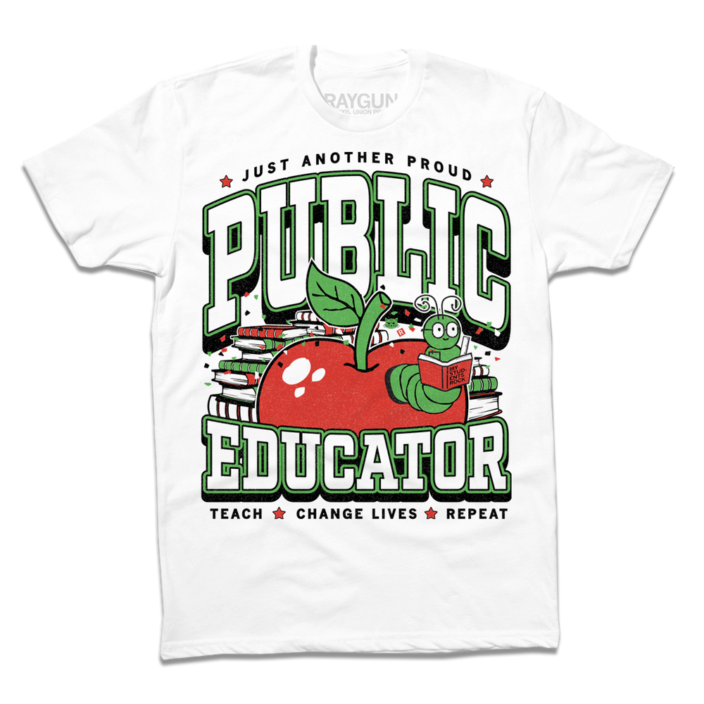 A white tee with text in black, green, and white that reads "Just another proud public educator. Teach, change lives, repeat" around a red apply with a bookworm popping out and a stack of red & green books in the back.