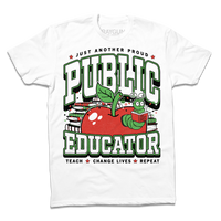 A white tee with text in black, green, and white that reads "Just another proud public educator. Teach, change lives, repeat" around a red apply with a bookworm popping out and a stack of red & green books in the back.