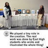 Two young women stand on either side of a table displaying framed portrait artwork of Waterloo Women at an East High School event.
