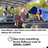Annie DiRusso performs on an outdoor stage at GRRRL CAMP 2024, singing and playing a red electric guitar while wearing a lime green RAYGUN t-shirt.