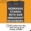 A charcoal gray, union-made t-shirt with the white text NEBRASKA STANDS WITH OUR IMMIGRANT NEIGHBORS printed on the front.