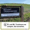 A sign that reads Welcome to Mount Trashmore, Elevation 948 in front of a grassy hill, shown on a Cedar Rapids T-shirt.