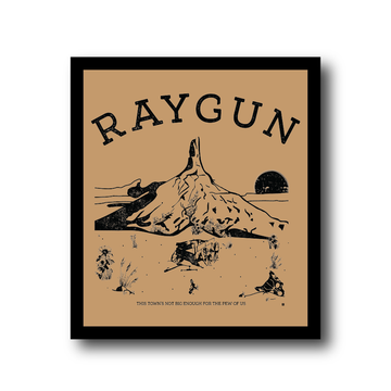 Framed RAYGUN art print of a desert landscape with a lone rock formation, a wagon, and the text THIS TOWNS NOT BIG ENOUGH FOR THE PEW OF US.