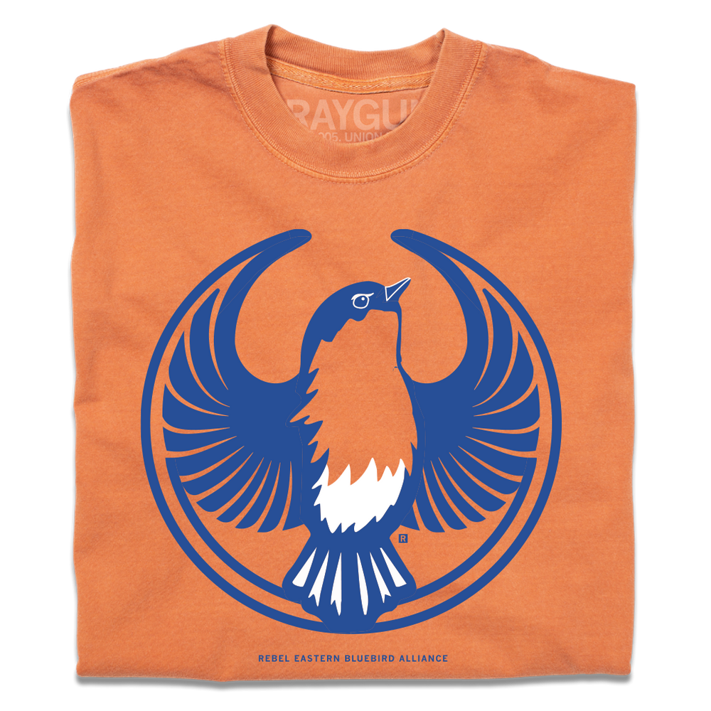 A folded heavyweight orange shirt with the Rebel Eastern Bluebird Alliance Logo. It uses a eastern bluebird with outstretched wings to mimic the shape of the Star Wars Rebel Alliance Logo. The eastern bluebird is printed in blue & white ink.