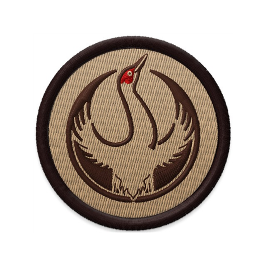An embroidered circular patch with the Rebel Sandhill Crane Alliance Logo. It uses a rebel sandhill crane with outstretched wings to mimic the shape of the Star Wars Rebel Alliance Logo. The bird is printed in red and brown. The edge of the patch i s dark brown and the background is tan.