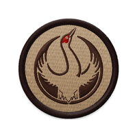 An embroidered circular patch with the Rebel Sandhill Crane Alliance Logo. It uses a rebel sandhill crane with outstretched wings to mimic the shape of the Star Wars Rebel Alliance Logo. The bird is printed in red and brown. The edge of the patch i s dark brown and the background is tan.