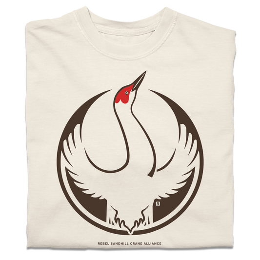 A folded heavyweight ivory t-shirt with the Rebel Sandhill Crane Alliance Logo. It uses a rebel sandhill crane with outstretched wings to mimic the shape of the Star Wars Rebel Alliance Logo. The bird is printed in red and brown ink.