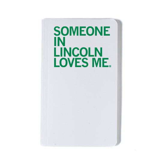 A white notebook featuring emerald green screen print text that reads, SOMEONE IN LINCOLN LOVES ME.