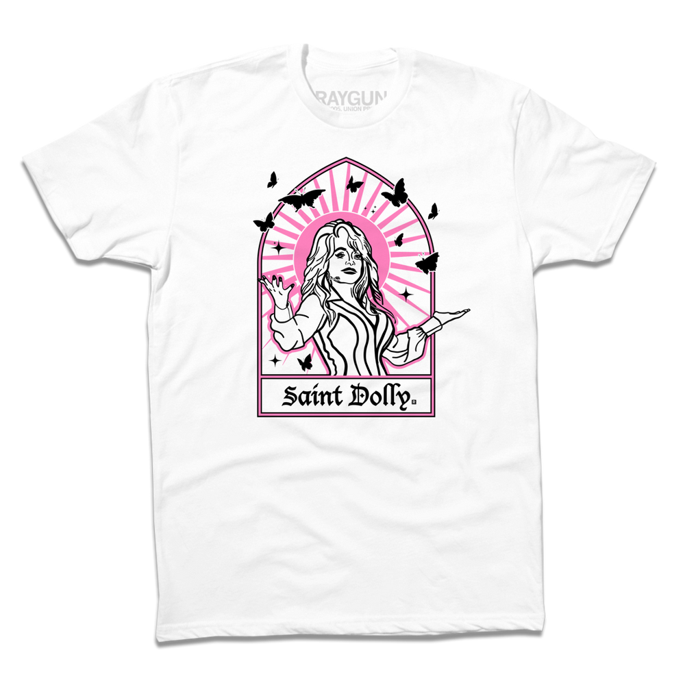 Short sleeve white t-shirt with pink & black print depicting Dolly Parton with her arms outstretched. A stained glass frame is around her, with a pink sun behind her, black butterflies around her, and text at the bottom that says, "SAINT DOLLY."