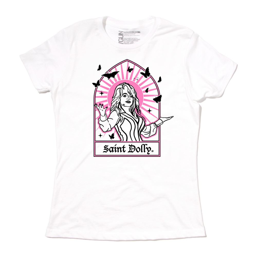 Women's size white t-shirt with pink & black print depicting Dolly Parton with her arms outstretched. A stained glass frame is around her, with a pink sun behind her, black butterflies around her, and text at the bottom that says, "SAINT DOLLY."