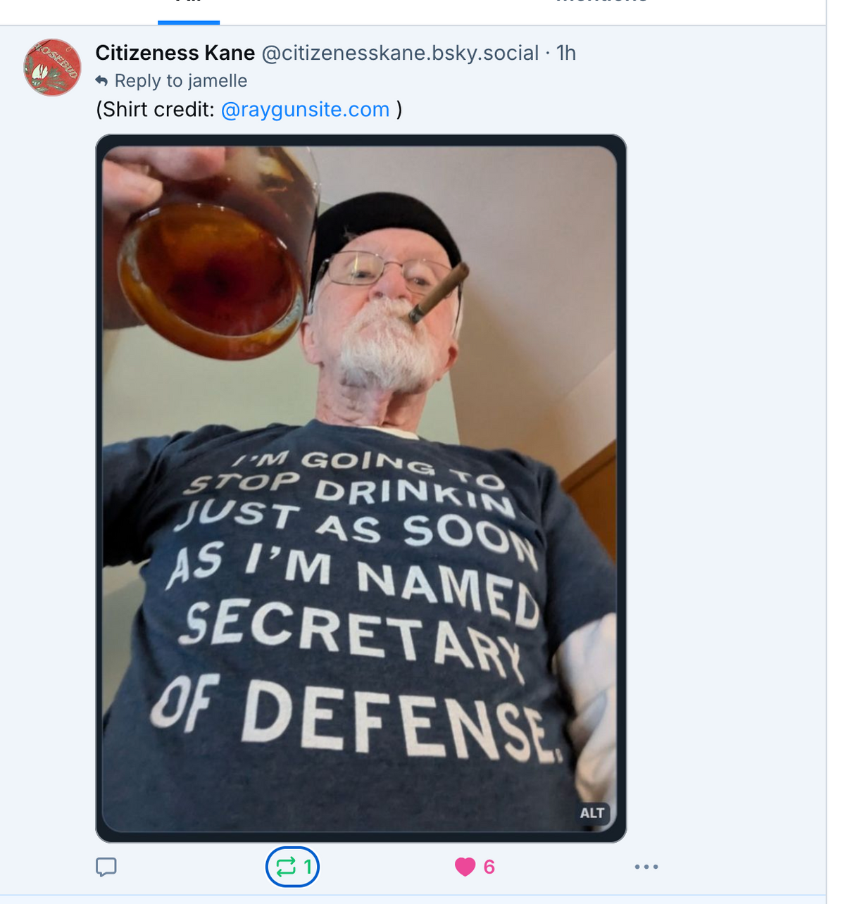 A man with a white goatee and glasses wears a RAYGUN t-shirt that reads, Im going to stop drinkin just as soon as Im named Secretary of Defense, while holding a glass of amber liquid and smoking a cigar.
