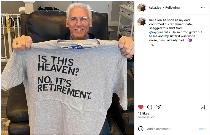 A man in glasses holds up a union made, gray retirement t-shirt that reads, Is this heaven? No, its retirement.