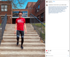 A man wearing sunglasses and a red AMERICA NEEDS TEACHERS t-shirt walks down a set of concrete steps in front of a brick school building, highlighting his support for public education.