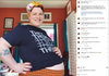 A smiling pregnant person wearing a headscarf and a gender pronoun T-shirt with the words THEY THEM printed repeatedly, posing with their hands on their hips and belly.