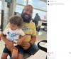 A bearded man in a yellow CAT El Cat Train shirt holds a toddler in a matching kids white t-shirt while sitting in an airport terminal.