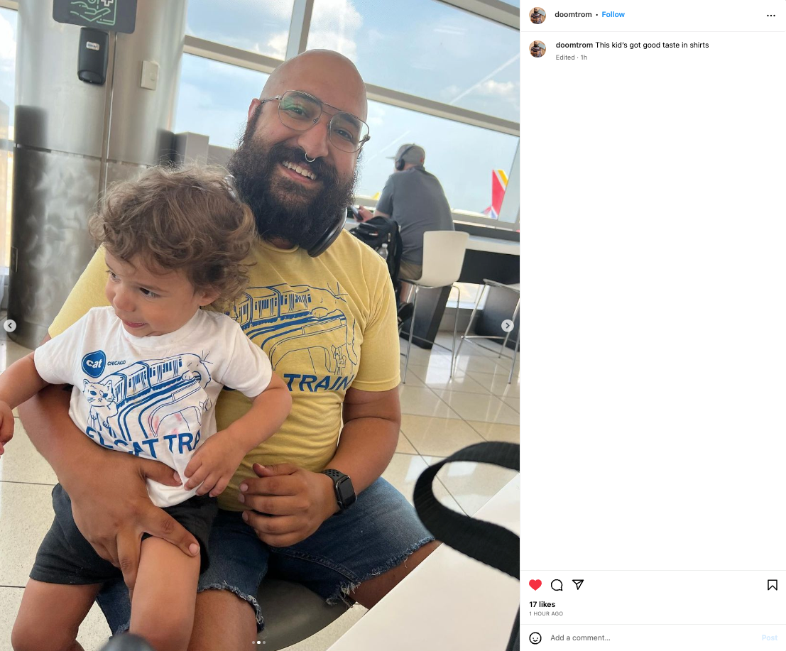 A bearded man in a yellow CAT El Cat Train shirt holds a toddler in a matching kids white t-shirt while sitting in an airport terminal.