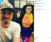 A man in a baseball cap and a woman wearing glasses, a black hat, and a yellow shirt that reads Say Gay Every Day pose for a selfie while wearing supportive pride apparel.