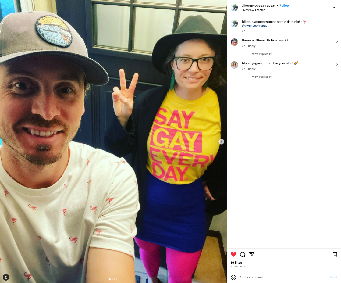 A man in a baseball cap and a woman wearing glasses, a black hat, and a yellow shirt that reads Say Gay Every Day pose for a selfie while wearing supportive pride apparel.